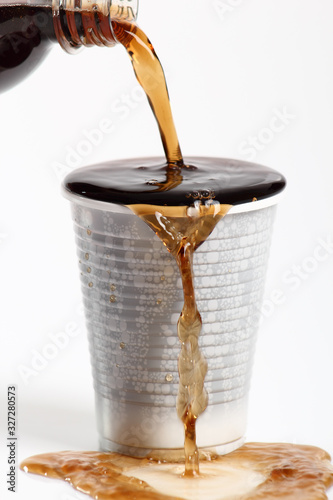 Pouring cola from bottle into overflowing plastic cup. Isolated on white background.