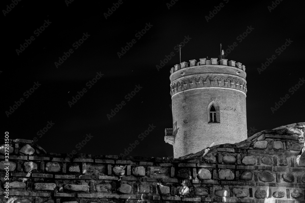 Black and white composition of medieval ruin of a watch tower at night with fence in the foreground