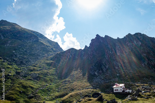 Sun casting rays on a mountain rescue house with mountain and puffy clouds in the background