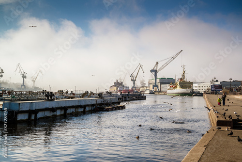 The embankment of the Neva with an icebreaker, cranes and seagulls on a foggy spring warm day in April