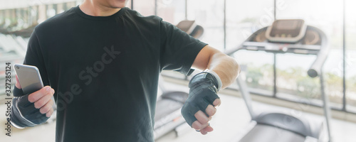 Asian athletes man wearing fitness gloves are resting after exercising. And use a smartphone with smartwatch to checking health data.Concept of sport and technology.