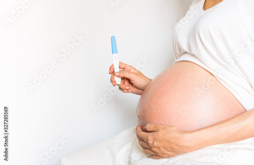 Pregnant women wearing white shirts, hand holding pregnancy test with two stripes positive result. holding pregnancy test with two stripes positive result.