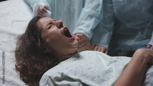 young mother screams and cries during childbirth, maternity hospital, strong pain, caucasian woman contractions, obstetricians gynecologists and midwives support