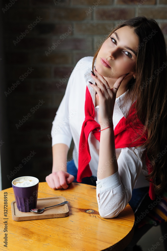 Girl at a table by the window in a cafe with a cup of coffee Girl at a table by the window in a cafe with a cup of coffee