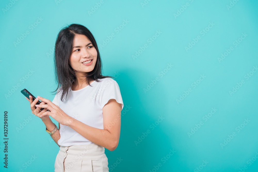 Woman standing smile, holding mobile phone looking back to space Woman standing smile, holding mobile phone looking back to space