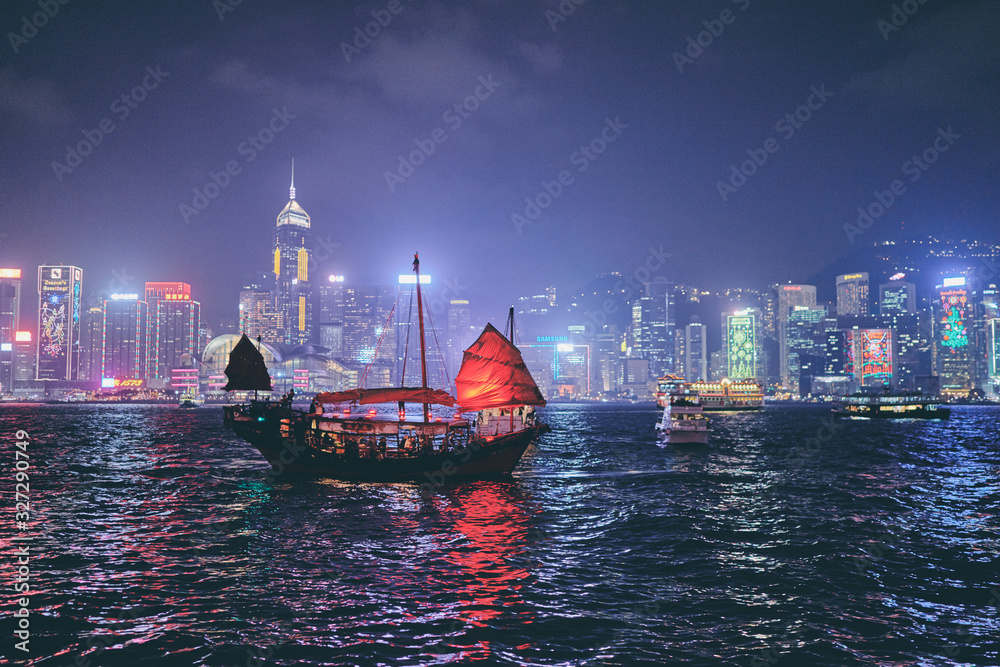 Naklejka premium Victoria Harbour Hong Kong night view with junk ship on foreground.