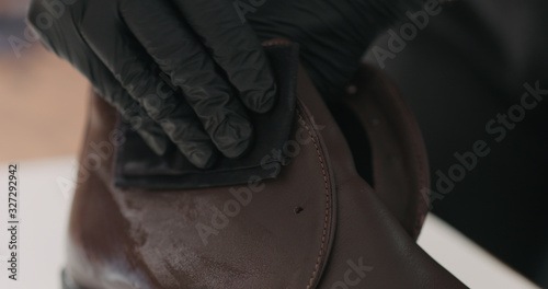 man hands in black gloves applying protective cream to brown leather chukka boots