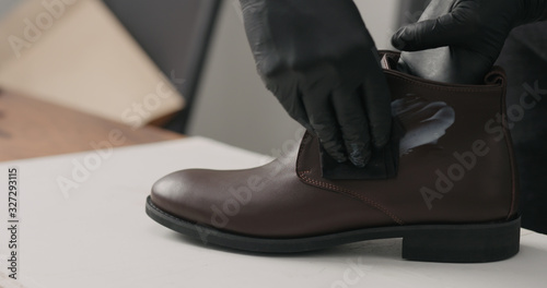 man hands in black gloves applying protective cream to brown leather chukka boots