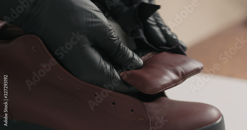 man hands in black gloves applying protective cream to brown leather sneakers
