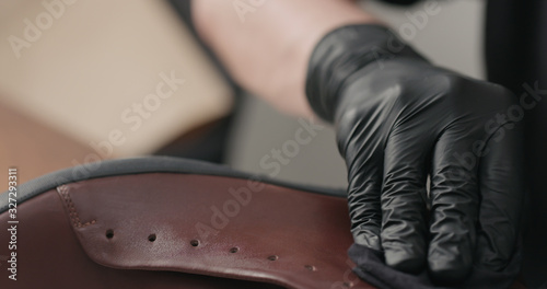 man hands in black gloves applying protective cream to brown leather sneakers