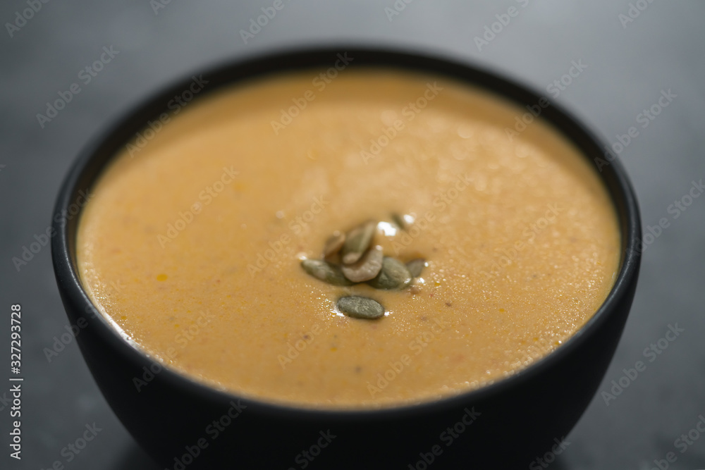 Pumpkin cream soup with pumpkin seeds in a black bowl on concrete background Pumpkin cream soup with pumpkin seeds in a black bowl on concrete background
