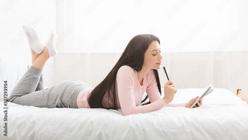 Young woman with pen and notebook writing to-do-list n bed Young woman with pen and notebook writing to-do-list n bed