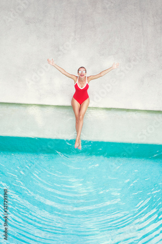Enjoying suntan and vacation. Top view of excited young woman in red swimsuit rising hands up near swimming pool. © luengo_ua