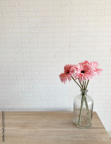 Fototapeta Naklejka Na Ścianę i Meble -  Pink daisy flower in glass vase on wooden table, effect light