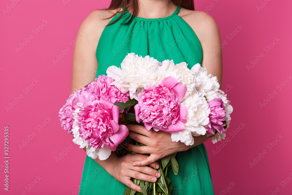 Faceless portait of slim woman holds beautiful bouquet of white and pink peonies in front of his her while standing isolated over pink studio ackground, lady with flowers for international women's day