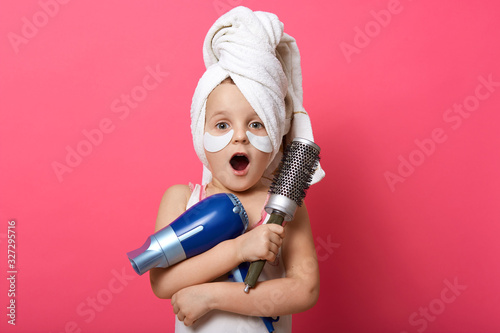 Fotobehang Close up portrait of beautiful little astonished girl with hair dryer and brush
