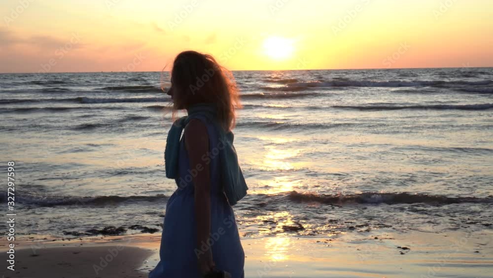 Active woman with sandals in hands walking near coastline of sea Active woman with sandals in hands walking near coastline of sea