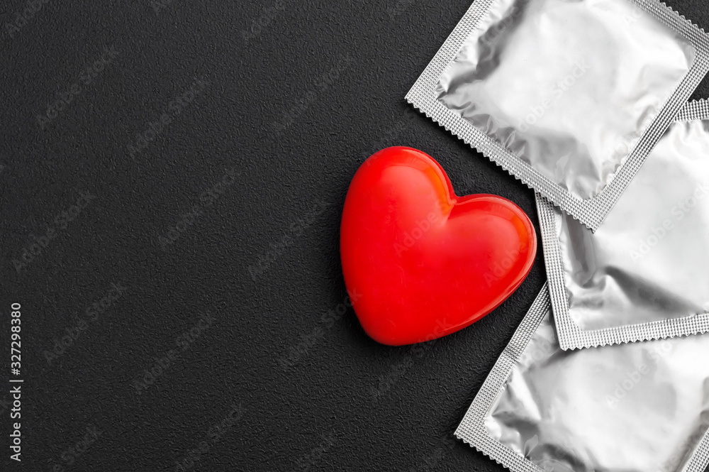 Obraz premium Red heart with condoms on black background. Safe sex concept.
