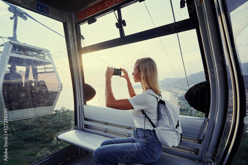 Traveling by Turkey. Young tourist woman sitting in Alanya's cable car enjoying view taking photo on her smartphone.