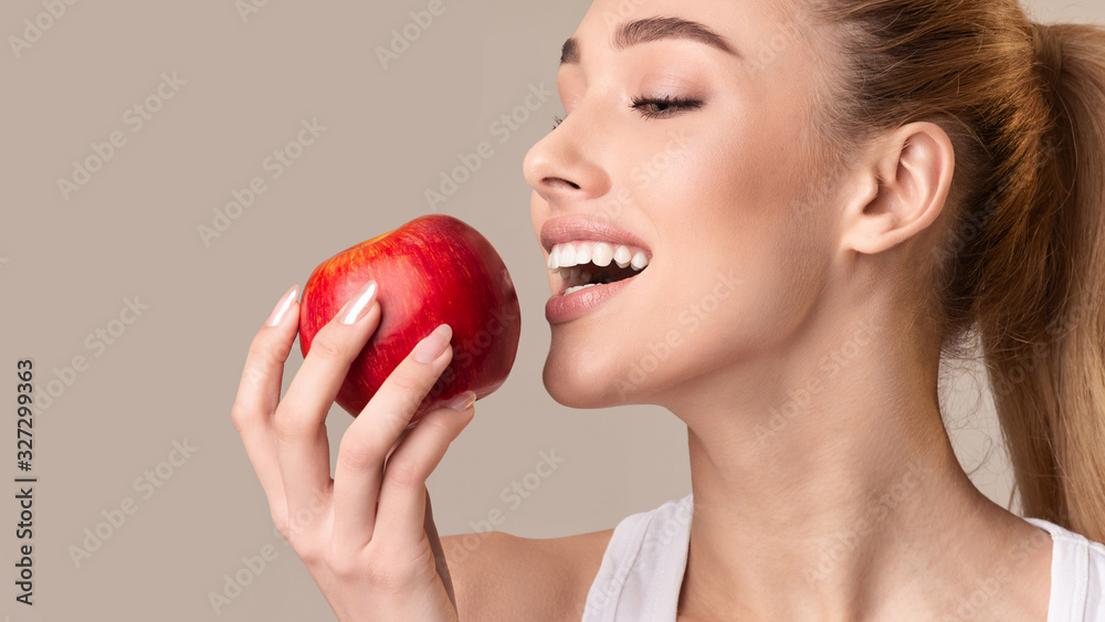 Young Lady Biting Red Apple On Beige Studio Background, Panorama Young Lady Biting Red Apple On Beige Studio Background, Panorama