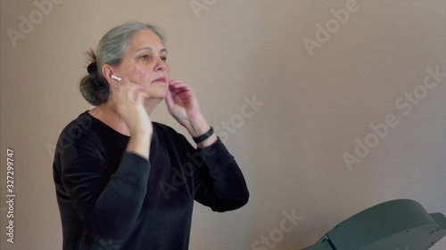  Woman put on wireless headphones walks on a treadmill and listening to music, aerobic exercise and endurance training at home.