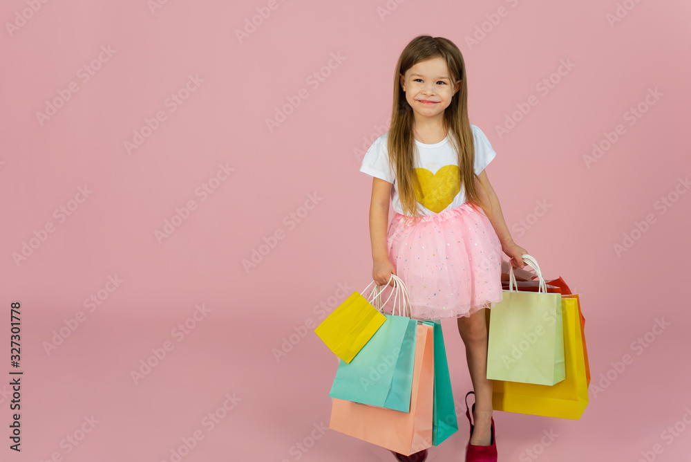 Girl with many shopping bags on pastel pink backgound. Lovely sweet moments of little princess, pretty friendly child having fun to camera Girl with many shopping bags on pastel pink backgound. Lovely sweet moments of little princess, pretty friendly child having fun to camera