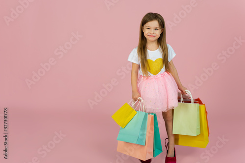 Girl with many shopping bags on pastel pink backgound. Lovely sweet moments of little princess, pretty friendly child having fun to camera