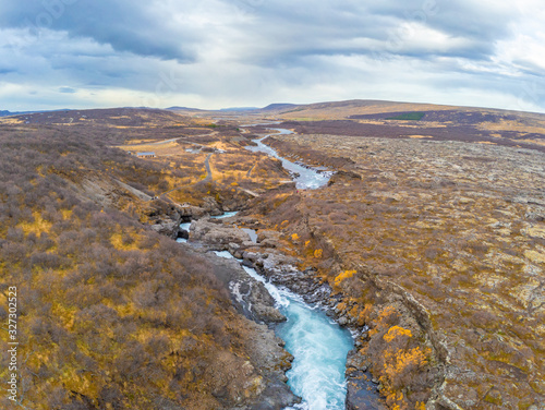 Hraunfossar series of waterfalls barnafoss aerial image of turquoise water streaming down gaps in lava field during autumn photo