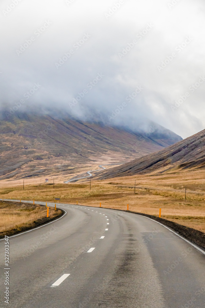 Northern Iceland empty road winding through valley upwards a mountain during grey weather