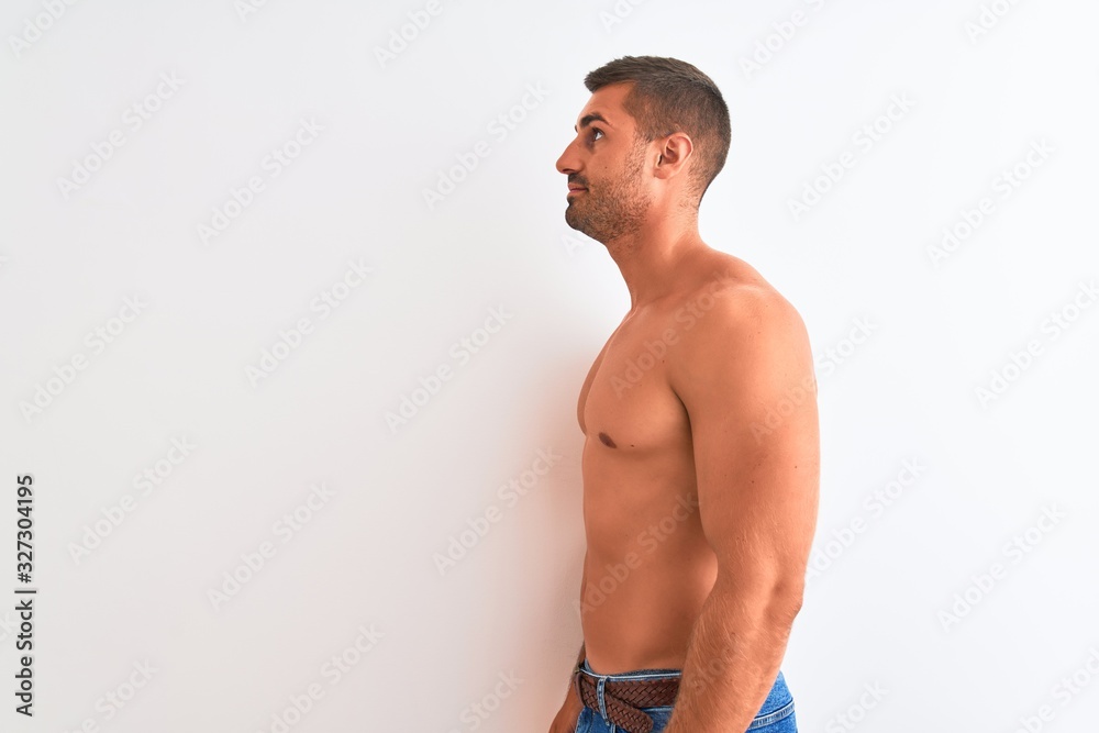 Young handsome shirtless man showing muscular body over isolated background looking to side, relax profile pose with natural face with confident smile.