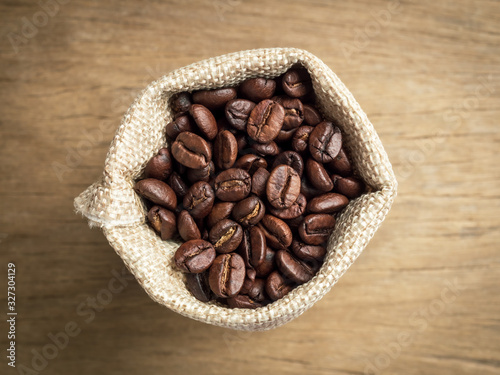 Close-up and top view of roasted coffee beans in sack bag on wooden background.