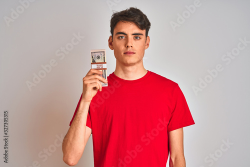 Teenager boy holding a bunch of dollars bank notes over isolated background with a confident expression on smart face thinking serious