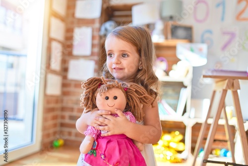 Obraz na plátně Adorable blonde toddler hugigng doll around lots of toys at kindergarten