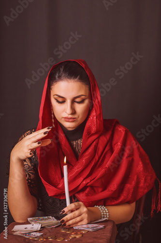 Woman with a scarf on her head and with cards in her hands divines over a candle and coins