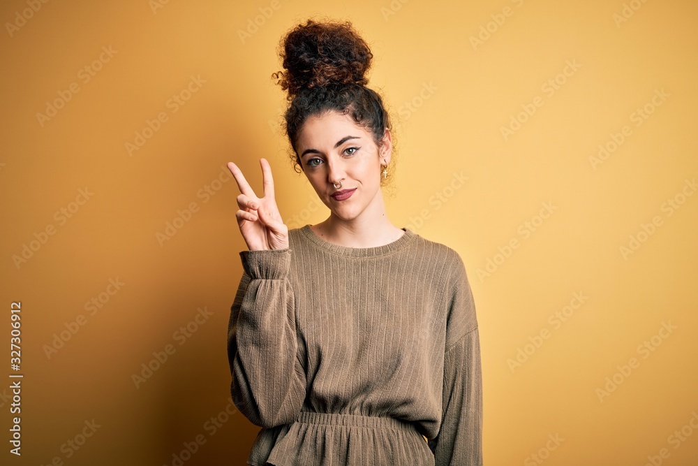 Young beautiful brunette woman with curly hair and piercing wearing casual dress showing and pointing up with fingers number two while smiling confident and happy. Young beautiful brunette woman with curly hair and piercing wearing casual dress showing and pointing up with fingers number two while smiling confident and happy.