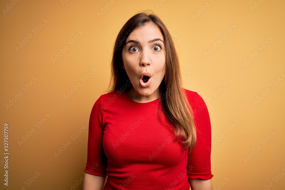 Beautiful young woman wearing casual red t-shirt over yellow isolated background afraid and shocked with surprise expression, fear and excited face. Beautiful young woman wearing casual red t-shirt over yellow isolated background afraid and shocked with surprise expression, fear and excited face.