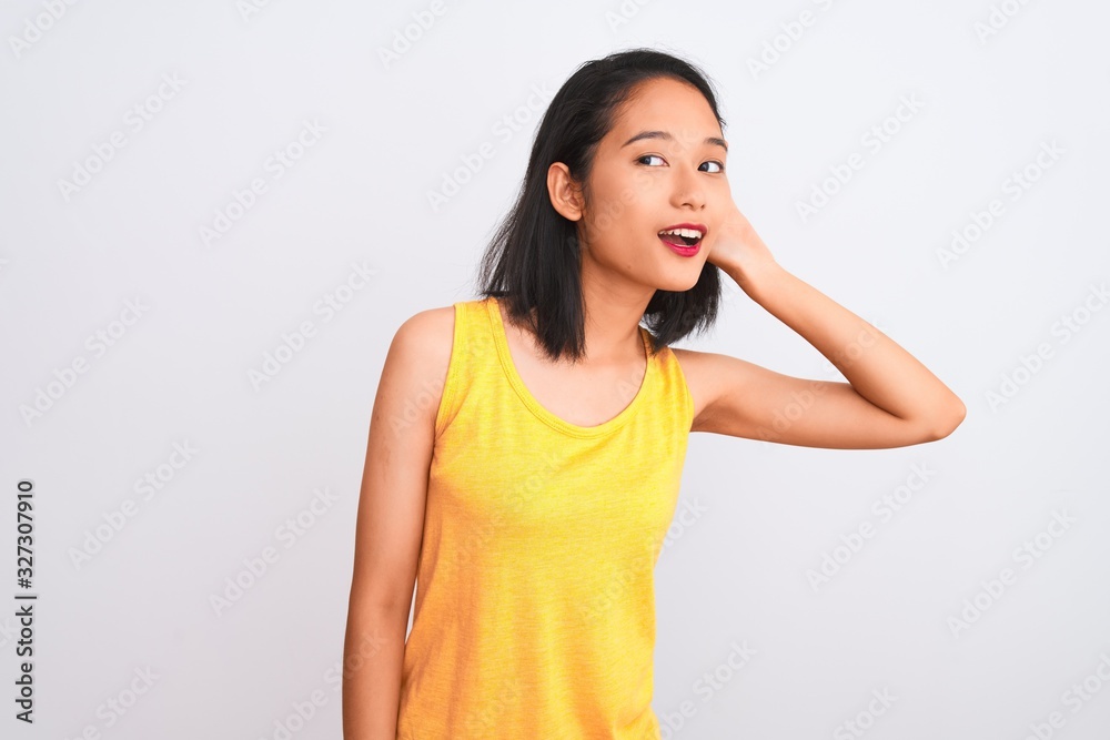 Young chinese woman wearing yellow casual t-shirt standing over isolated white background smiling with hand over ear listening an hearing to rumor or gossip. Deafness concept. Young chinese woman wearing yellow casual t-shirt standing over isolated white background smiling with hand over ear listening an hearing to rumor or gossip. Deafness concept.