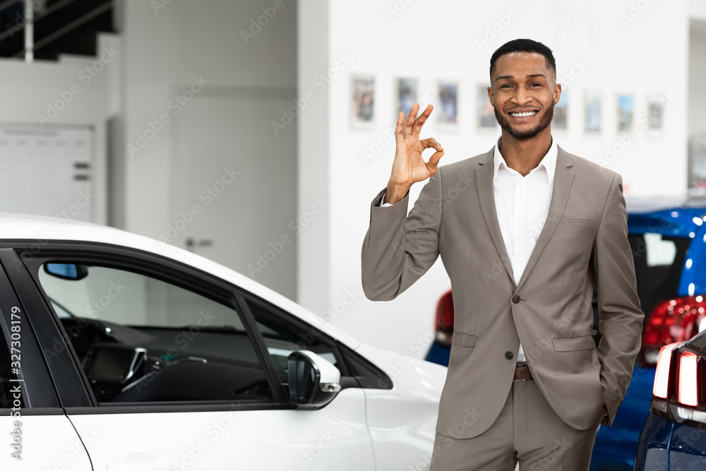 Smiling Salesman Gesturing Okay Standing In Luxury Auto Store Smiling Salesman Gesturing Okay Standing In Luxury Auto Store