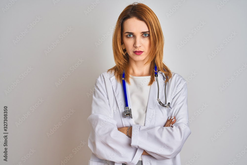 Redhead caucasian doctor woman wearing stethoscope over isolated background skeptic and nervous, disapproving expression on face with crossed arms. Negative person. Redhead caucasian doctor woman wearing stethoscope over isolated background skeptic and nervous, disapproving expression on face with crossed arms. Negative person.