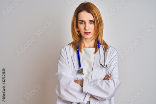Redhead caucasian doctor woman wearing stethoscope over isolated background skeptic and nervous, disapproving expression on face with crossed arms. Negative person.
