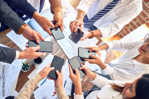 Group of business workers standing with hands together using smartphone doing symbol at the office © Krakenimages.com