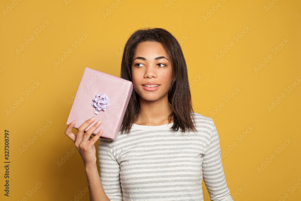 Pretty black girl holding pink gift box on colorful yellow background Pretty black girl holding pink gift box on colorful yellow background
