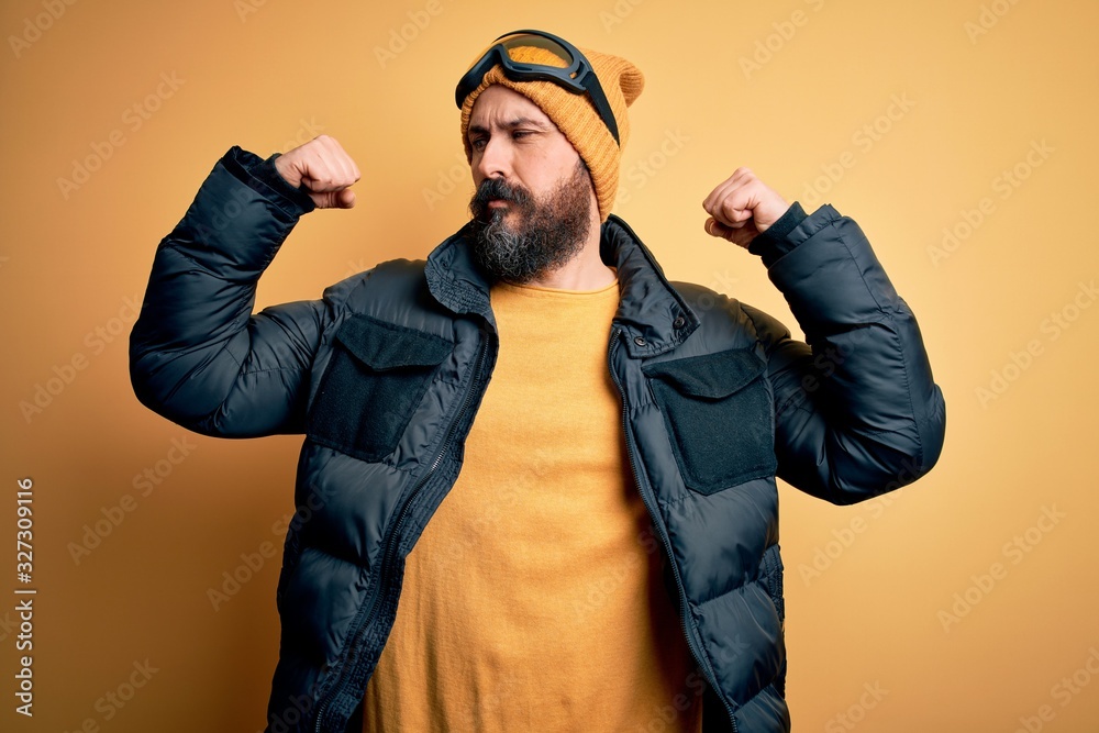 Handsome skier bald man with beard skiing wearing snow sportswear and ski goggles showing arms muscles smiling proud. Fitness concept. Handsome skier bald man with beard skiing wearing snow sportswear and ski goggles showing arms muscles smiling proud. Fitness concept.