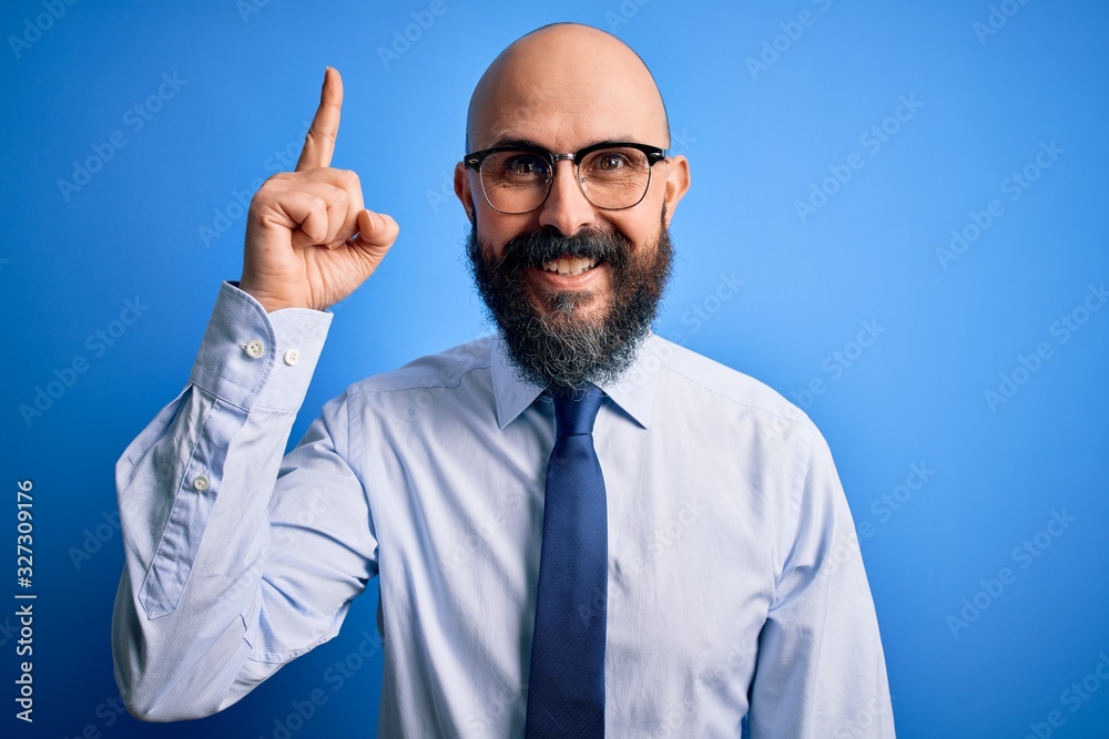 Handsome business bald man with beard wearing elegant tie and glasses over blue background pointing finger up with successful idea. Exited and happy. Number one. Handsome business bald man with beard wearing elegant tie and glasses over blue background pointing finger up with successful idea. Exited and happy. Number one.