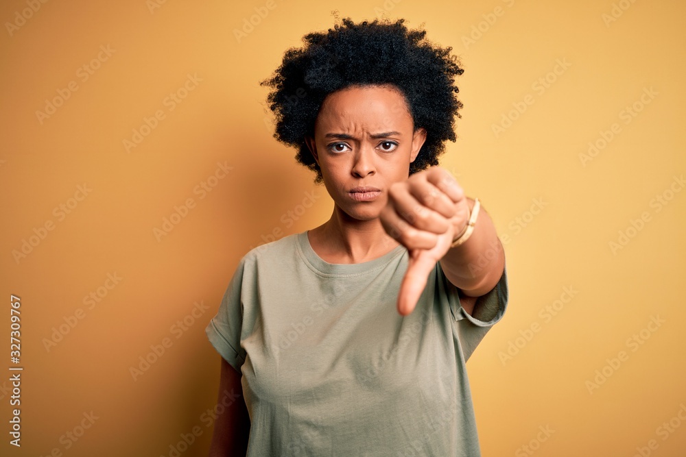 Young beautiful African American afro woman with curly hair wearing casual t-shirt looking unhappy and angry showing rejection and negative with thumbs down gesture. Bad expression. Young beautiful African American afro woman with curly hair wearing casual t-shirt looking unhappy and angry showing rejection and negative with thumbs down gesture. Bad expression.