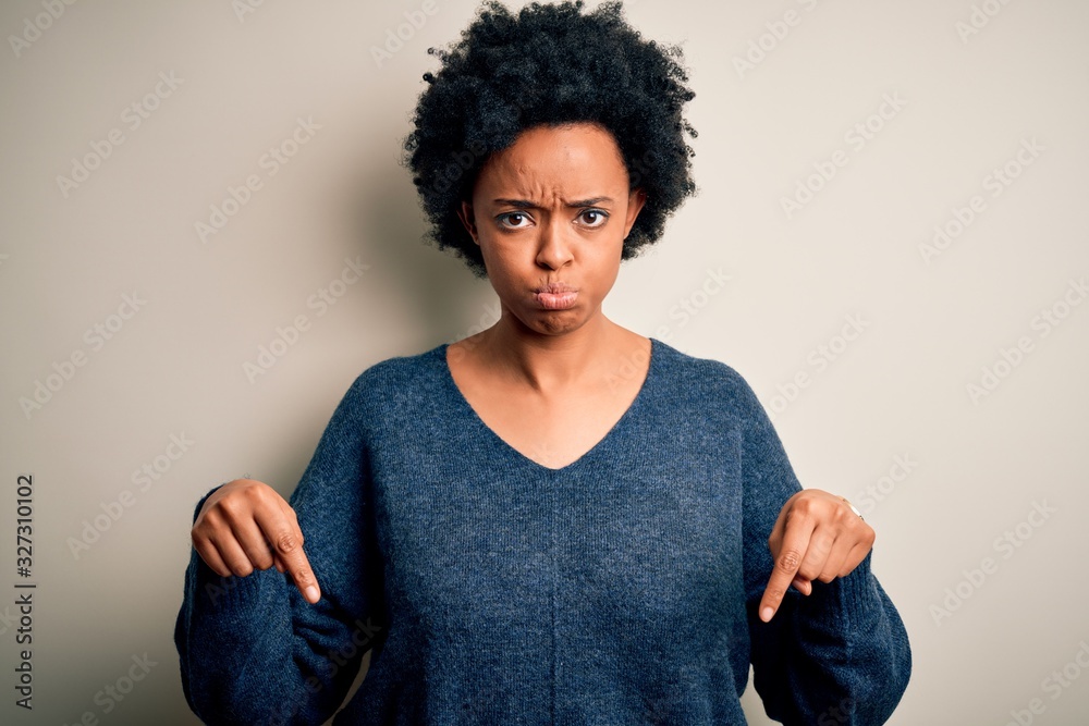 Young beautiful African American afro woman with curly hair wearing casual sweater Pointing down looking sad and upset, indicating direction with fingers, unhappy and depressed. Young beautiful African American afro woman with curly hair wearing casual sweater Pointing down looking sad and upset, indicating direction with fingers, unhappy and depressed.