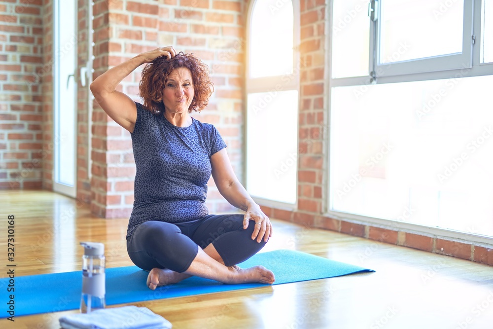 Middle age beautiful sportswoman wearing sportswear sitting on mat practicing yoga at home confuse and wonder about question. Uncertain with doubt, thinking with hand on head. Pensive concept. Middle age beautiful sportswoman wearing sportswear sitting on mat practicing yoga at home confuse and wonder about question. Uncertain with doubt, thinking with hand on head. Pensive concept.