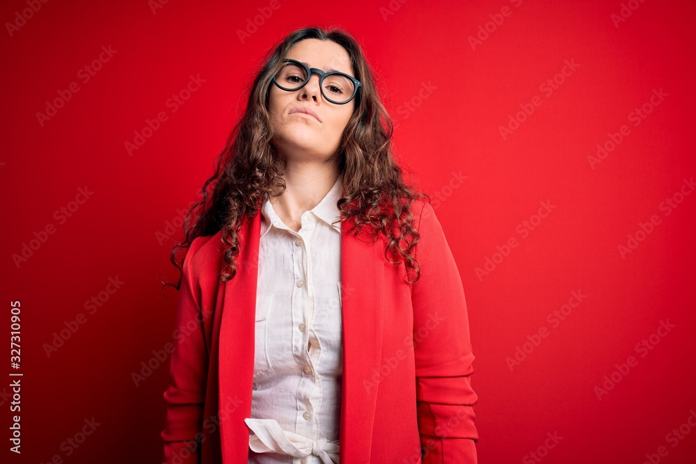 Young beautiful woman with curly hair wearing jacket and glasses over red background Relaxed with serious expression on face. Simple and natural looking at the camera. Young beautiful woman with curly hair wearing jacket and glasses over red background Relaxed with serious expression on face. Simple and natural looking at the camera.
