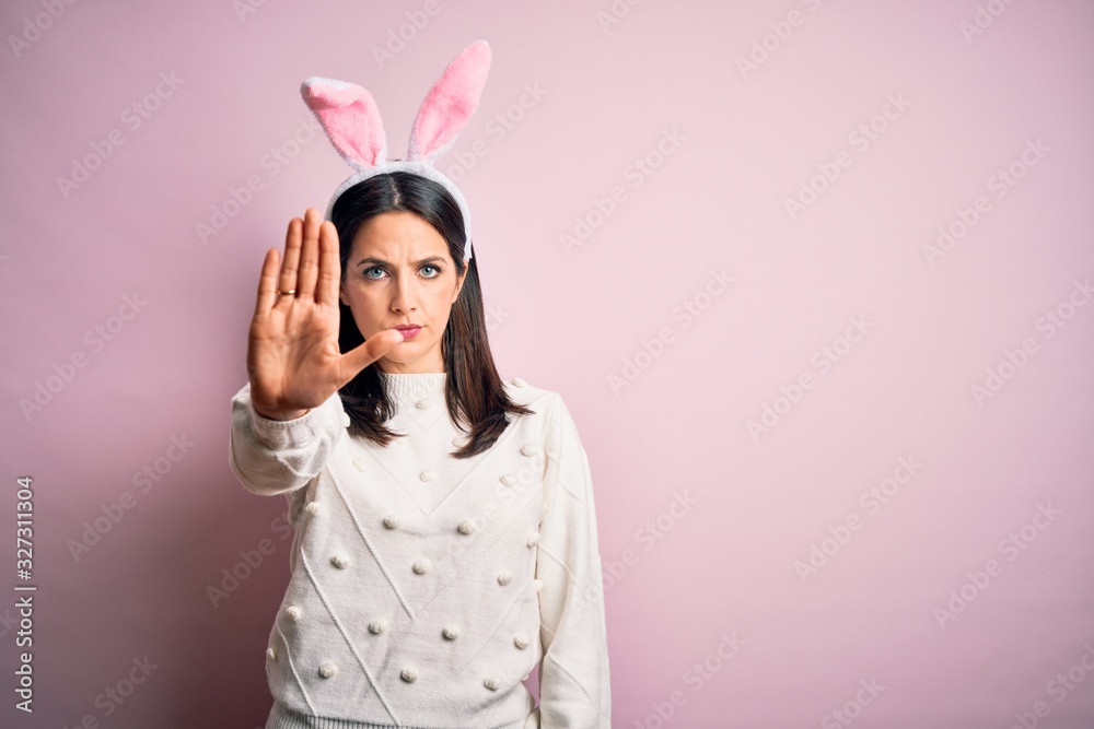 Young caucasian woman wearing cute easter rabbit ears over pink isolated background doing stop sing with palm of the hand. Warning expression with negative and serious gesture on the face.