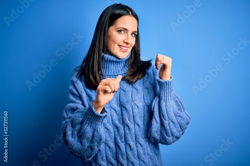 Young brunette woman with blue eyes wearing casual turtleneck sweater Pointing to the back behind with hand and thumbs up, smiling confident photo